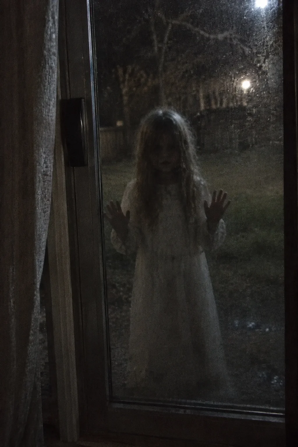 Illustration of a pale girl in a white dress with her hands pressed against a glass door at night
