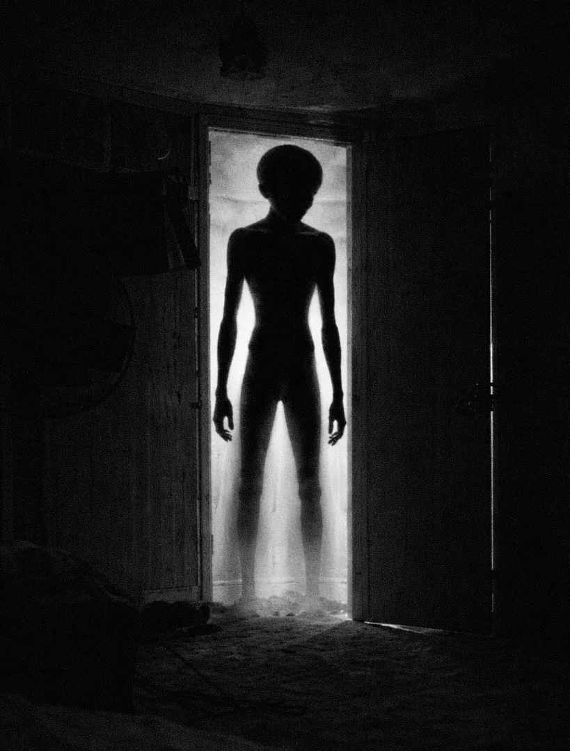 Depiction of a tall black humanoid silhouette in a doorway