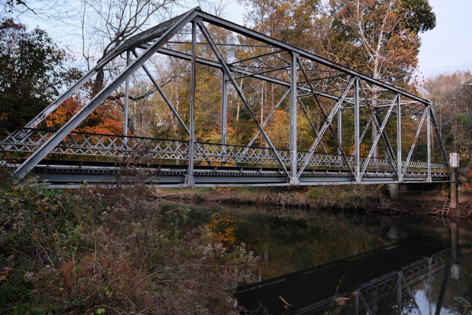 A steel truss bridge over a creek surrounded by autumn trees
